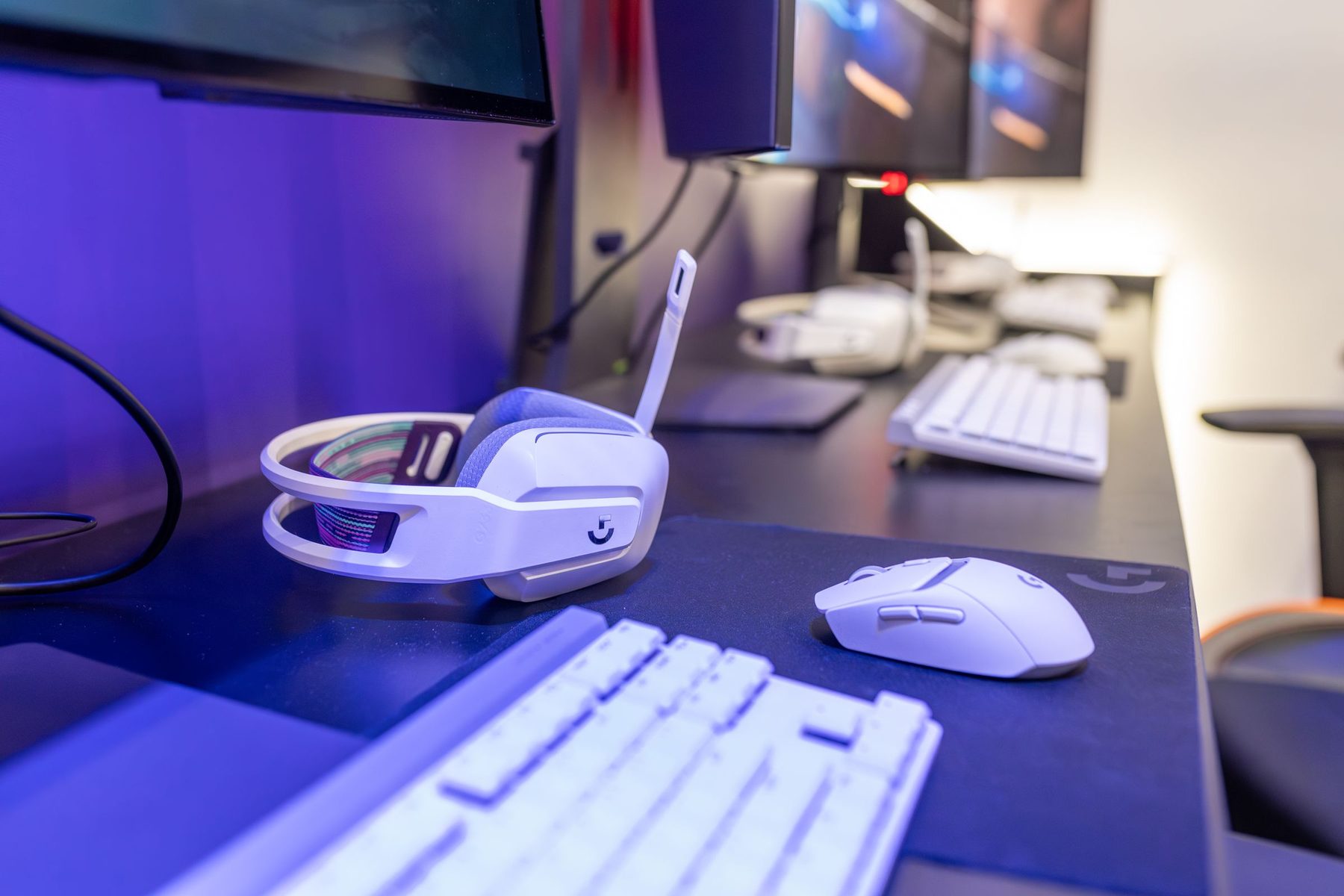 Skrivebord med tastatur, mus og et hvidt gaming-headset i blåt lys